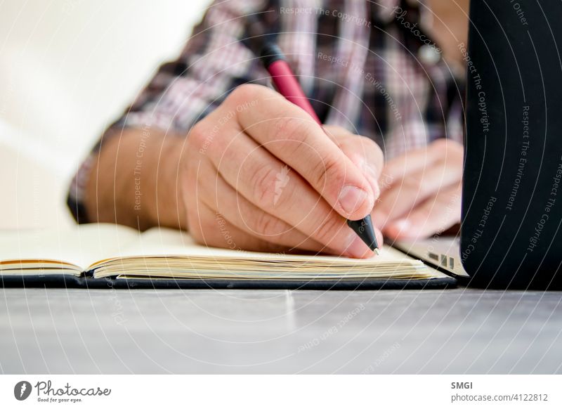 Ein Mann schreibt in ein Notebook neben einem Laptop E-Learning Person Bildung Computer Lernen online Business heimwärts Technik & Technologie studierend