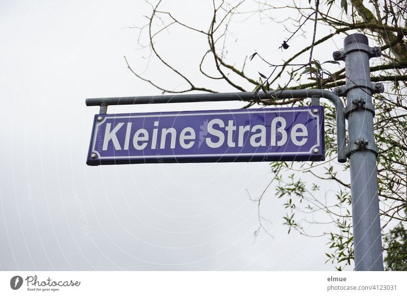 blaues Straßenschild " Kleine Straße "  an einer Metallstange vor einem Baum / Straßenname Schild Schilder & Markierungen Strassenschild Buchstaben