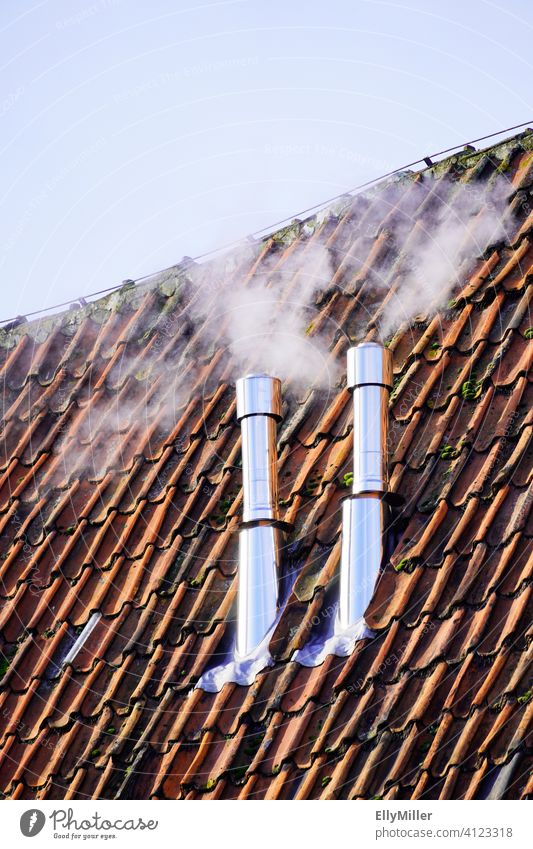 Zwei rauchende Schornsteine an einem alten Dach mit roten Dachziegeln. Rauch heizen Wärme Energie wärme abgebend wärmeerzeugung Qualm Edelstahl Rohr Heizung