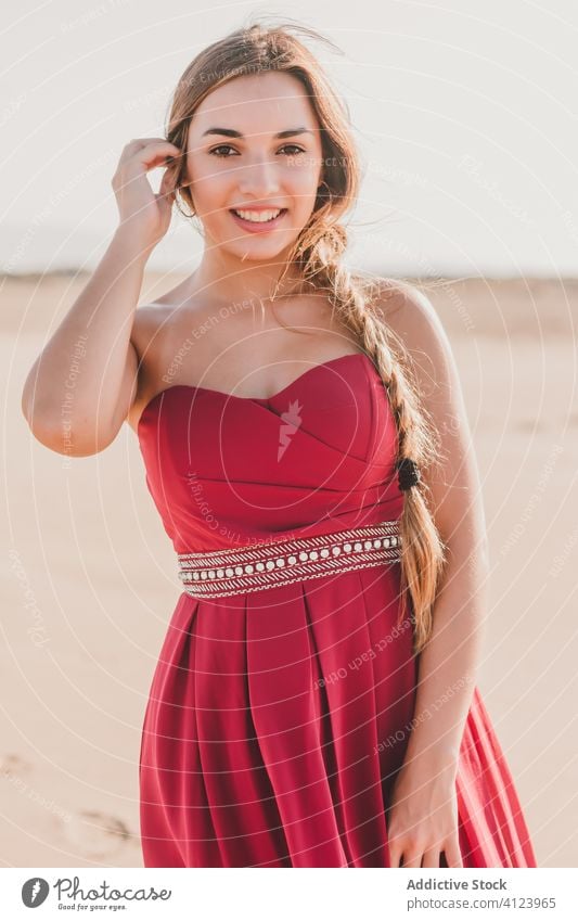 Positive junge Frau in stilvollem roten Kleid am Sandstrand stehend Küste Stil charmant sinnlich blond träumen romantisch Freiheit positiv Lächeln Sommer