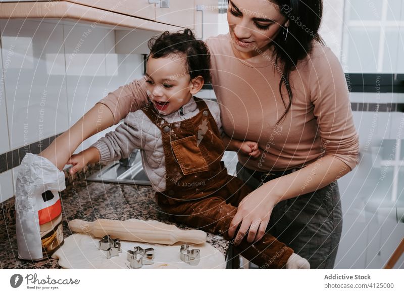 Fröhliche Mutter beim Backen von Gebäck mit kleinem Sohn in der Küche Koch Nudelholz Teigwaren Keks Helfer Assistent Zusammensein Bonden Liebe Stuhl Kind heiter