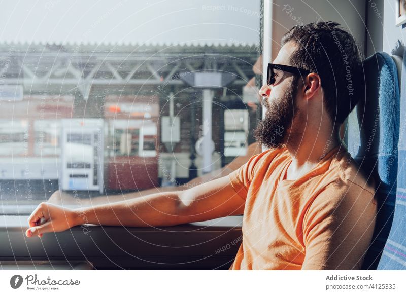 Nachdenklicher junger bärtiger Mann schaut durchs Fenster, während er mit dem Zug reist Ausflug reisen träumen besinnlich Sonnenlicht Sommer ernst Verkehr