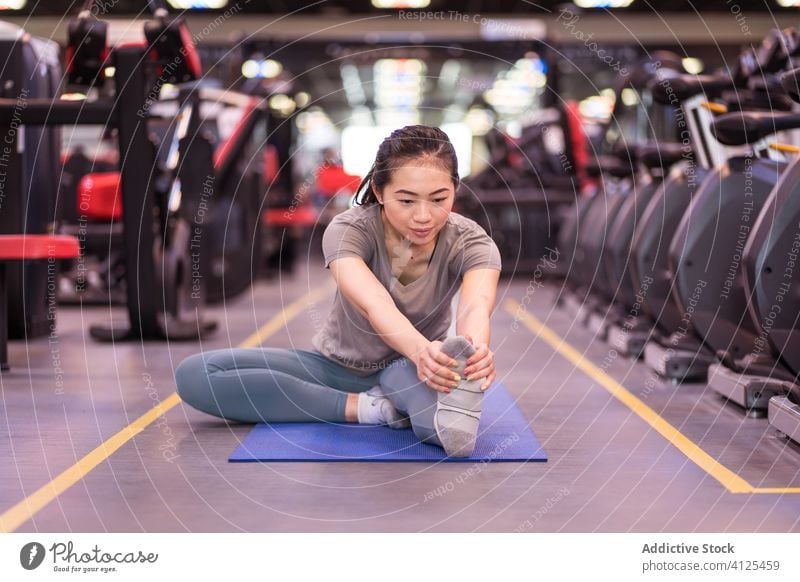 Starke junge ethnische Sportlerin, die ihre Beine auf einer Matte im Fitnessstudio streckt Unterlage Dehnung Training Aufwärmen passen Club schlank schlanke