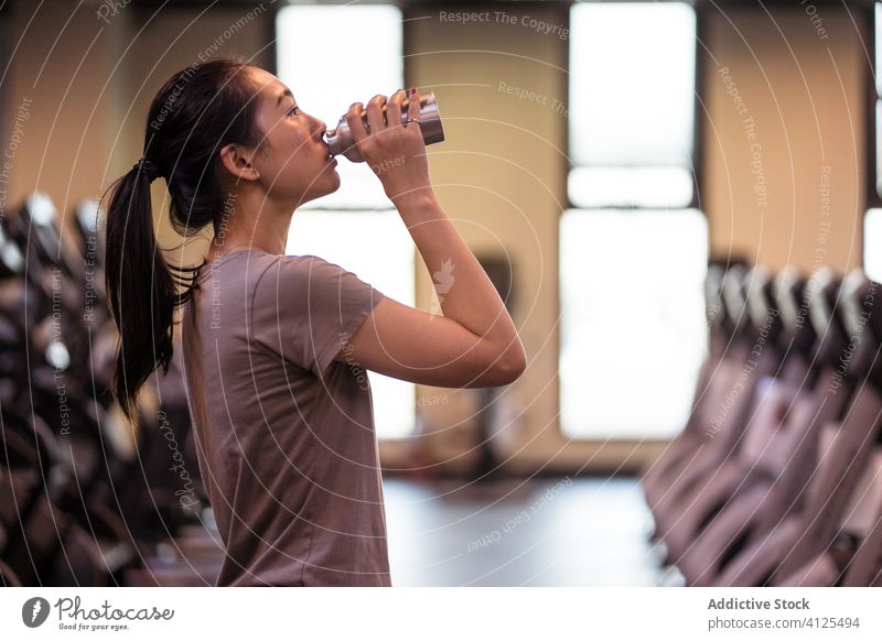 Junge ethnische Sportlerin trinkt Wasser aus einer Flasche im Fitnessstudio Frau trinken frisch Training Durst Hydrat Athlet Pause passen jung schlank