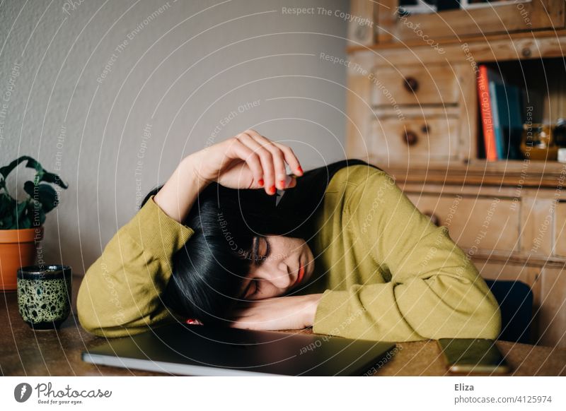 Eine Frau schläft zuhause am Tisch vor ihrem zugeklapptem Laptop Arbeit schlafen Home Office langweilig müde Mittagsschlaf Homeoffice Notebook erschöpft