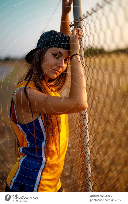 Sinnliche junge Frau steht in der Nähe von Metallzaun auf der Straße Zaun Sportbekleidung cool Generation modern Stil urban sportlich Uniform Verschlussdeckel