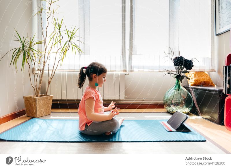 Barfuß Mädchen tun Meditation in gemütlichen Raum zu Hause Kind Yoga Lotus-Pose Konzentration Zen Sprit meditieren Tablette Tutorial Video Unterlage Frieden