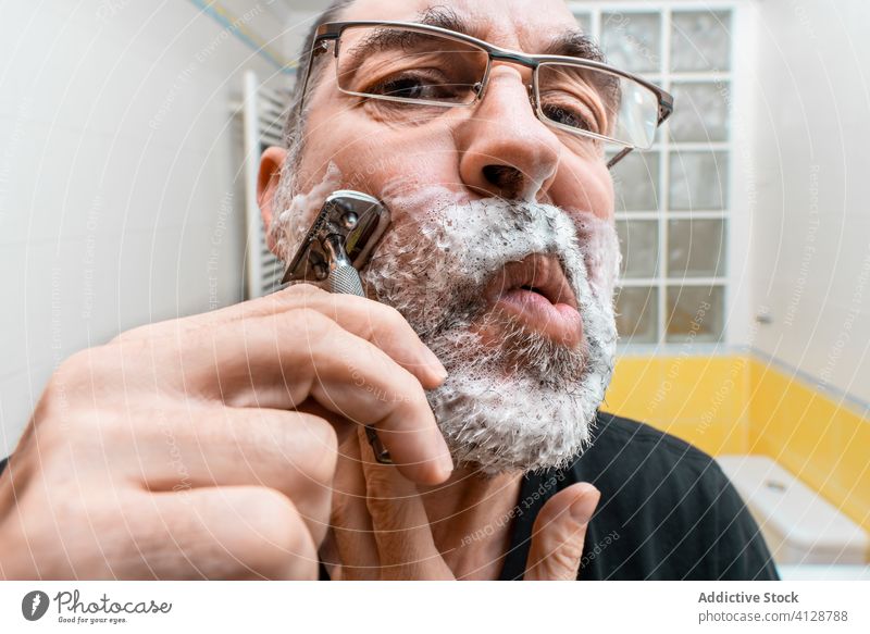 Bärtiger Mann beim Rasieren im Badezimmer Rasierer Einwegartikel Vollbart reif Verfahren Hygiene Pflege männlich Lebensmitte Routine Leckerbissen Werkzeug