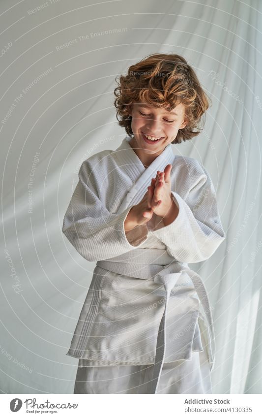 Positiver Junge in weißem Kimono, der zu Hause Judo übt Training Gurt kämpferisch Kunst Atelier Bestimmen Sie Lächeln selbstbewusst Sport positiv jung Kindheit
