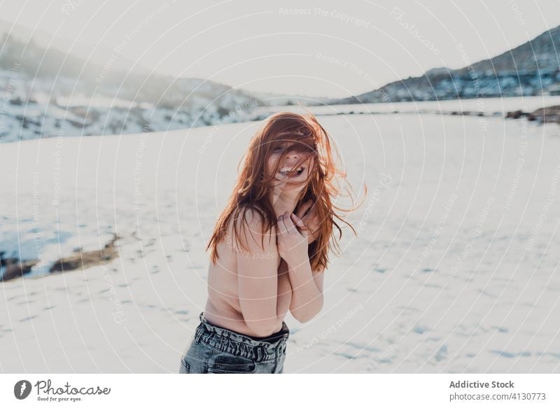 Junge Frau mit roten Haaren steht in einem verschneiten Feld rote Haare oben ohne Winter fliegendes Haar Natur Glück Schnee sich[Akk] entspannen Wind
