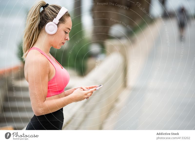 Sportliche Frau mit Kopfhörern, die soziale Medien auf ihrem Smartphone nutzt Sportlerin Sportbekleidung zuhören Musik Stauanlage MEER benutzend Apparatur Gerät