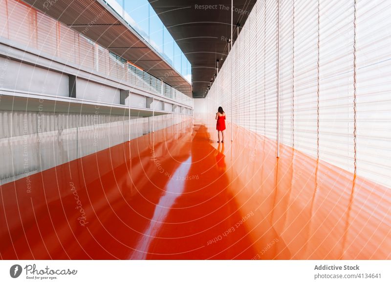 Anonyme Frau in geräumigem Korridor in minimalem Stil Gang Flur Innenbereich sehr wenige orange Farbe lebhaft Design Geometrie Durchgang futuristisch