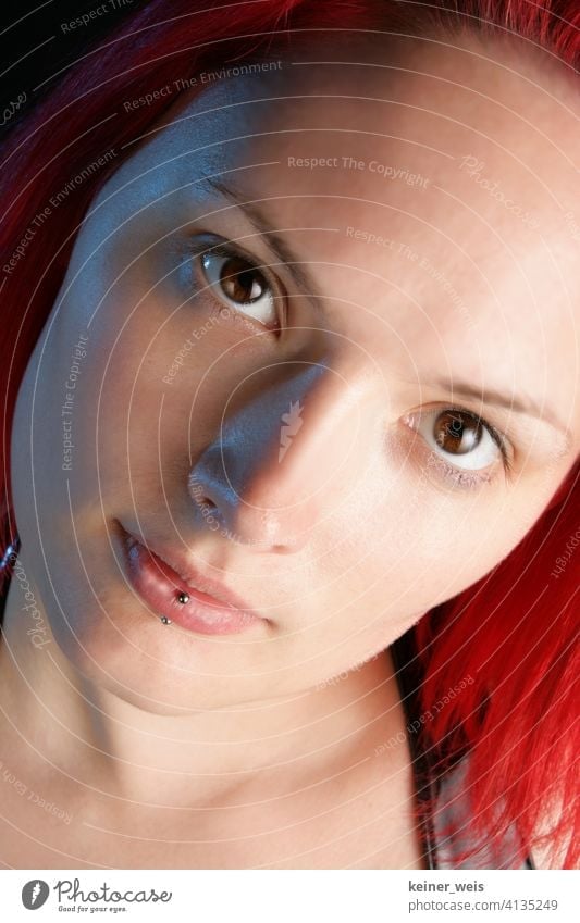 Gesicht einer jungen Frau mit Piercing in der Unterlippe und rotem Haar Lippenpiercing Junge Frau Hautschmuck braune Augen rothaarig rotes Haar hochformat