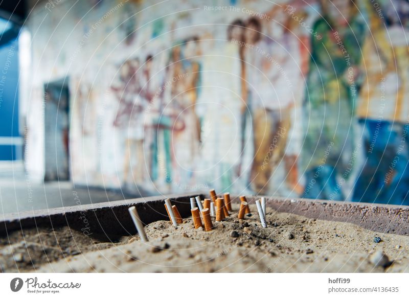 ausgedrückte Kippen im Sand vor bemalter Wand Zigarettenstummel Rauchen Tabakwaren Filterzigarette Zigarettenasche kippen ungesund Aschenbecher