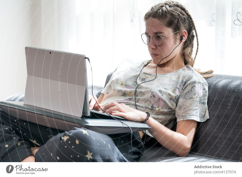 Junge Frau mit Kopfhörern am Laptop zu Hause heimwärts benutzend jung zuhören zuschauen Apparatur online Schüler lässig Video Gerät Internet Browsen Lifestyle