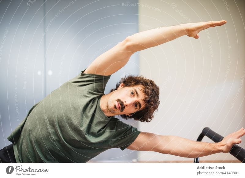 Flexibler Sportler, der sich auf dem Pilates-Reformer dehnt Seitenknick Maschine Training Dehnung Aktivität beweglich Übung männlich üben Gesundheit stark