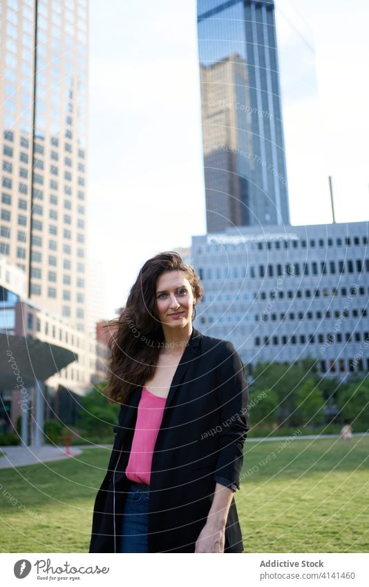 Entschlossene lächelnde Geschäftsfrau gegen Wolkenkratzer in der Innenstadt Stadtzentrum Bestimmen Sie professionell selbstbewusst Großstadt nachdenklich