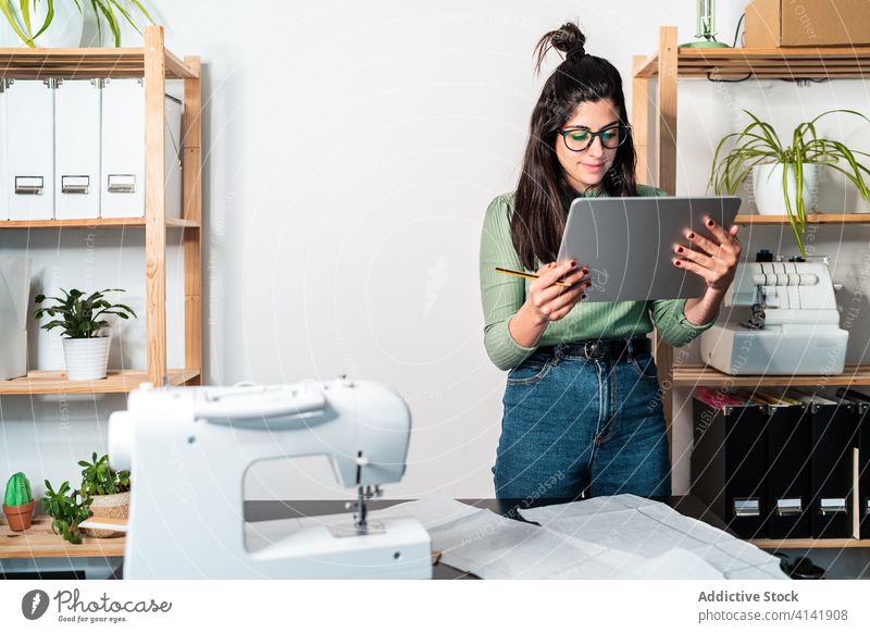 Schnittschneider mit Tabletten in der Nähe von Papieren und Nähmaschine Näherin messen Lineal Handwerk nach vorne lehnen Kleinunternehmen Arbeit Backsteinwand