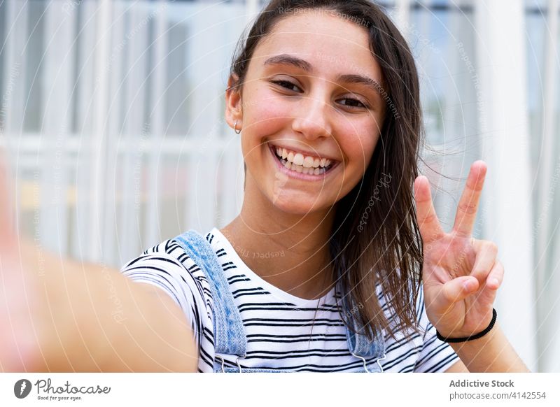 Fröhlicher Teenager gestikuliert mit V-Zeichen und macht ein Selfie v-Zeichen Lächeln Straße Großstadt Wochenende modern ruhen heiter Glück gestikulieren Freude