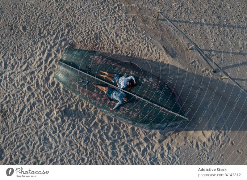 Entspanntes Paar, das sich auf einem umgestürzten Ruderboot am Strand ausruht sich[Akk] entspannen ruhen lässig hölzern auf den Kopf gestellt Sand romantisch