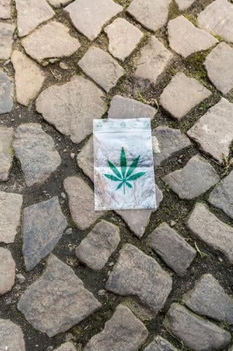 Cannabisblatt bedruckt auf einer kleinen Plastiktüte, die auf dem Bürgersteig liegt Sucht Hintergrund Tasche Blütenknospen Großstadt Kopfsteinpflaster