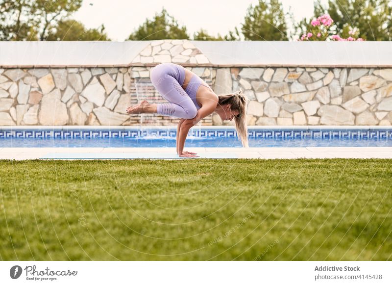 Flexible Frau beim Yoga in Kranichhaltung Kranichpose Bakasana Gleichgewicht üben Pose Asana Beckenrand Fokus aktive Kleidung Unterlage Wellness Sommer