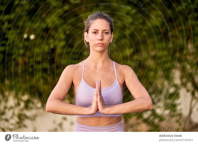 Ruhige Frau übt Yoga mit Namaste-Hände Geste Windstille ruhig Unterlage Hinterhof Hof gestikulieren BH Leggings schlank Wellness Asana üben Harmonie Gesundheit