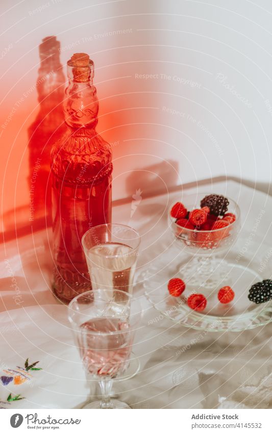 Glas Cocktail mit Beeren und Gläsern, serviert auf einem Tisch vor weißer Wand Flasche Teller trinken Zusammensetzung dienen Dekoration & Verzierung Design