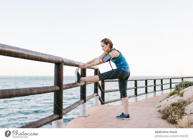 Schlanke Frau dehnt sich beim Training an der Strandpromenade Dehnung Aufwärmen MEER Hafengebiet schlank Athlet selbstbewusst Armbinde Spazierweg