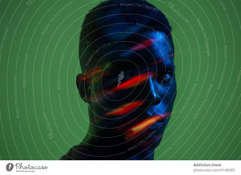 Junger schwarzer Mann mit Neonbeleuchtung im Gesicht selbstbewusst ernst jung neonfarbig modern kreativ farbenfroh Porträt Licht Afroamerikaner ethnisch