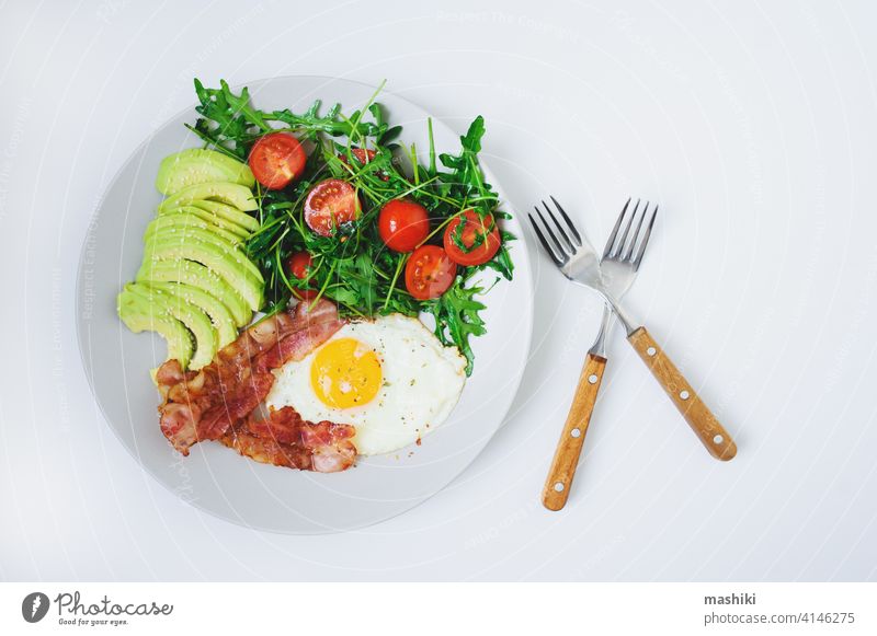 leckeres Frühstück - Spiegelei und Speck serviert mit Rucola-Tomaten-Salat und frischer Avocado auf weißem Teller Lebensmittel Mahlzeit Ei Morgen Gemüse Brunch