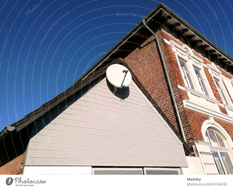 Satellitenschüsel im Spitzgiebel eines Nebengebäudes vor einem schönen Altbau im Sonnenschein in Lemgo bei Detmold in Ostwestfalen-Lippe Satellitenschüssel