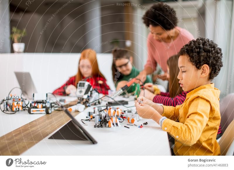 Glückliche Kinder mit ihren afroamerikanischen weiblichen Wissenschaft Lehrer mit Laptop Programmierung elektrische Spielzeuge und Roboter bei Robotik Klassenzimmer