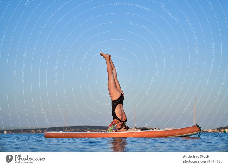 Unerkennbare Frau beim Yoga in gestützter Kopfstandposition Surfer Paddelbrett Asana Salamba sirsasana MEER Wasser erstaunlich Sonnenuntergang Dämmerung
