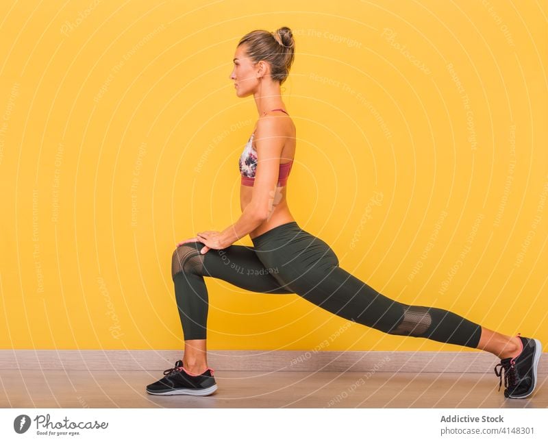 Sportliche Frau beim Training im modernen Fitnessstudio Ausfallschritte Übung Dehnung Aufwärmen üben pulsierend Farbe Leggings BH Sportlerin schlank Gesundheit