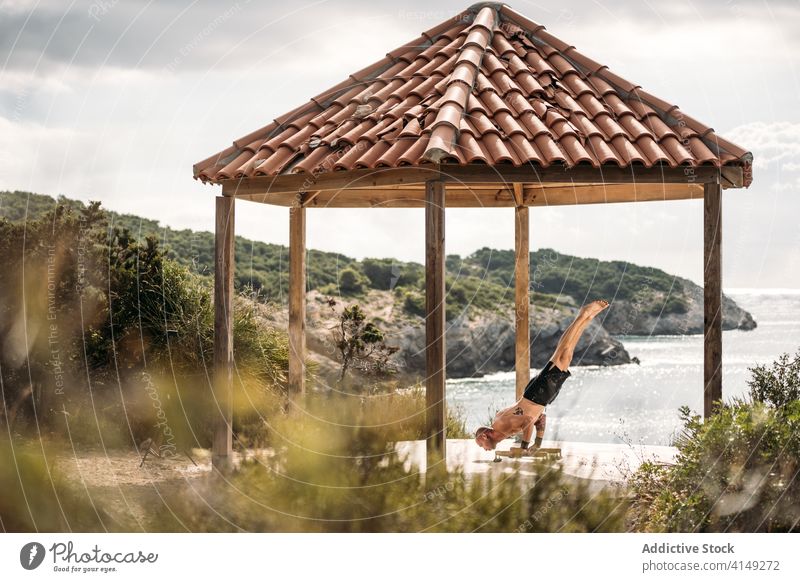 Sportlicher Mann beim Training auf einer Terrasse am Meer Handstand Gleichgewicht Sportler parallel Bar anstrengen Ausdauer Athlet männlich sonnig üben Sommer