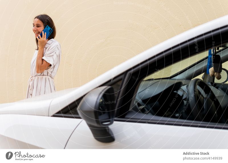 Lächelnde Frau, die in der Nähe eines Autos mit ihrem Smartphone spricht sprechen Fahrer parken Los PKW modern benutzend Gespräch Automobil Verkehr Fahrzeug