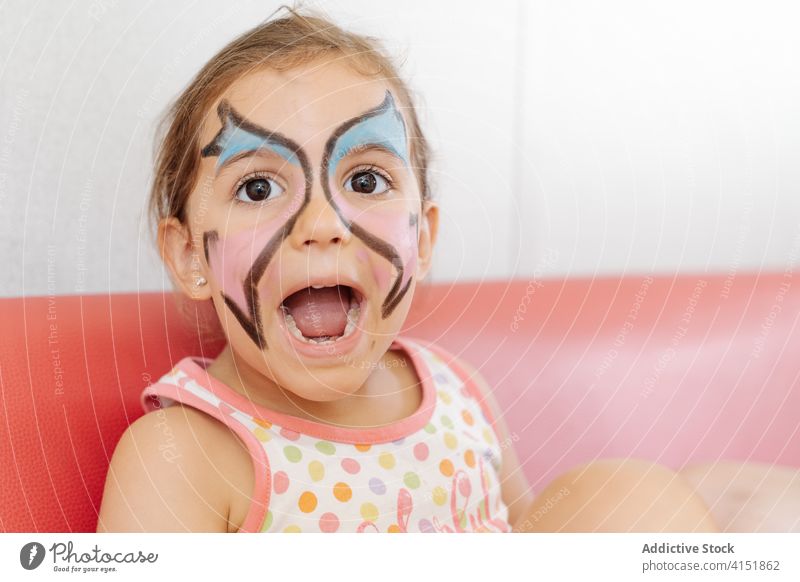 Glückliches Kind mit bemaltem Gesicht zu Hause Farbe Mädchen heimwärts Wochenende Spaß haben bezaubernd Bild Pigment Schmetterling Körperkunst Sofa heiter
