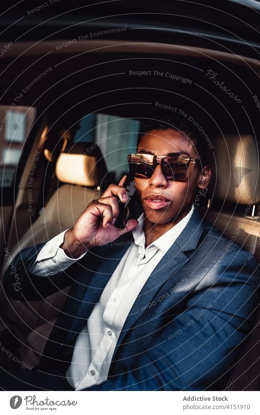 Lächelnder ethnischer Geschäftsmann, der im Auto mit seinem Smartphone spricht PKW Laufwerk reden Glück Kommunizieren positiv urban formal jung Mann