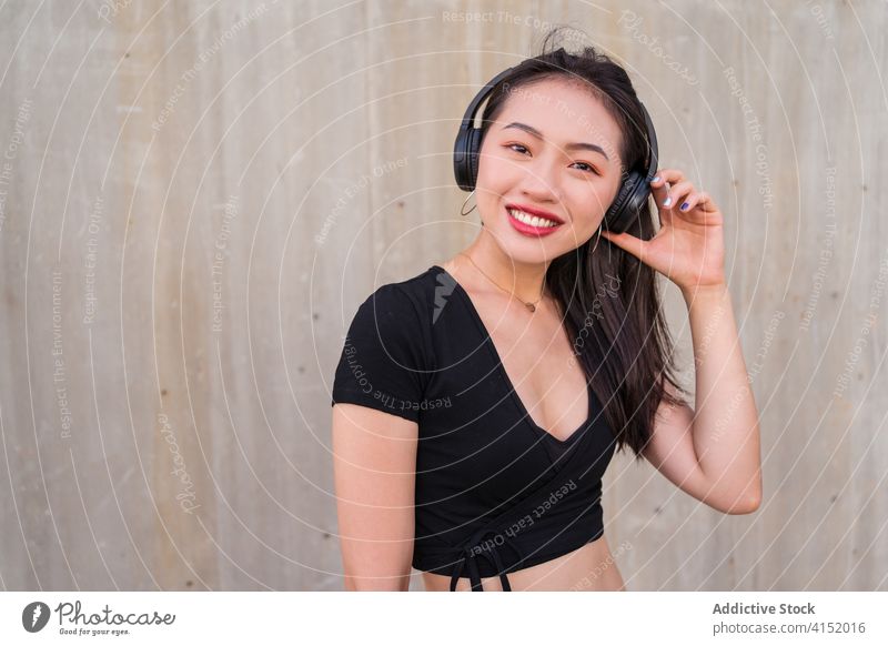 Unbekümmerte Frau, die mit Kopfhörern Musik hört zuhören sorgenfrei Smartphone benutzend genießen ethnisch asiatisch Glück heiter Freude Klang modern Apparatur