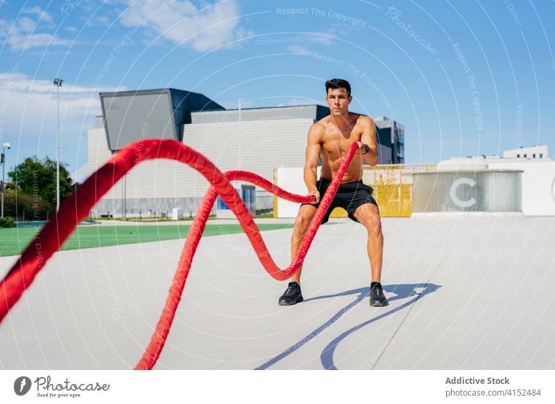 Starker Sportler beim Training mit Seilen Schlacht Übung Mann Terrasse sonnig stark männlich muskulös Athlet Fitness Gesundheit passen Sommer ohne Hemd Stärke