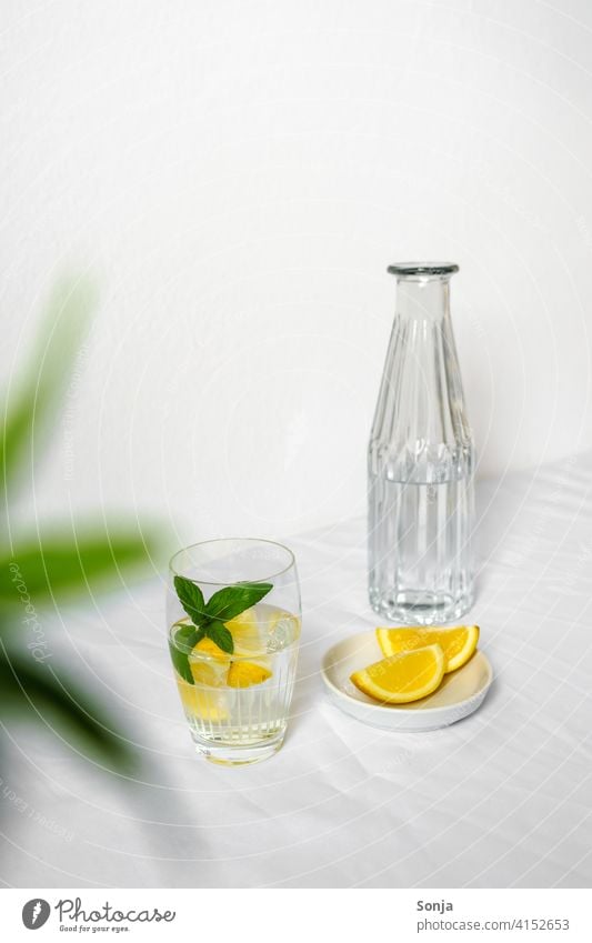 Eine Wasserflasche und ein Trinkglas mit Wasser, Zitrone und Pfefferminze auf einem weißen Tischtuch Erfrischungsgetränk Limonade gelb Zitronenscheibe Glas