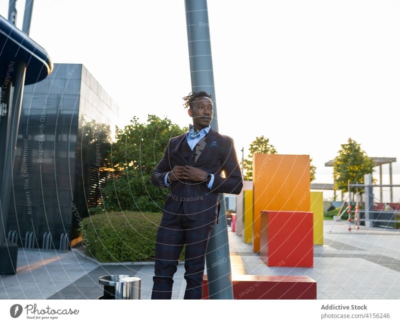 Selbstbewusster Geschäftsmann im stilvollen Anzug in der Stadt Großstadt Unternehmer Bestimmen Sie Lehnen ernst Straßenlaterne Sonnenlicht Stadtzentrum
