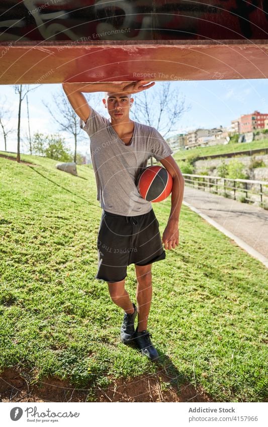 Sportlicher Mann mit Ball im Park stehend Sportler Training jung Athlet selbstbewusst Übung ethnisch männlich Bestimmen Sie Sportbekleidung Fitness Streetball