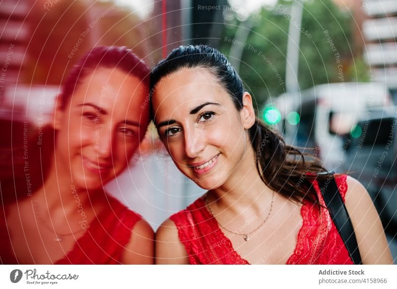 Glückliche ethnische Frau auf der Straße Lächeln urban Glaswand Reflexion & Spiegelung heiter modern freundlich jung hispanisch positiv Zeitgenosse Lifestyle
