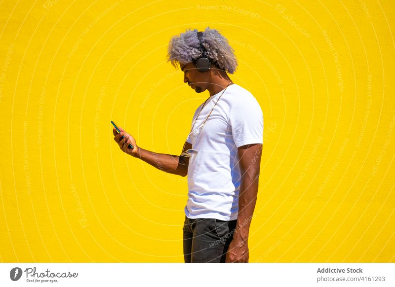Schwarzer Mann mit Afrofrisur hört Musik mit Kopfhörern auf einem Musik hören Afro-Look schwarz Musikhelme Musik abspielen gelber Hintergrund Afrohaar Mobile dj