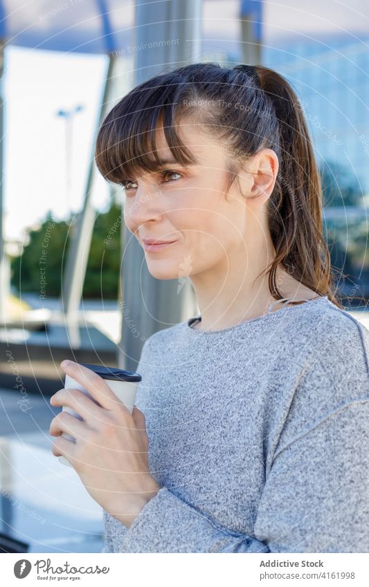 Glückliche junge Frau trinkt Kaffee zum Mitnehmen in der Nähe eines modernen Gebäudes Kaffeepause Straße positiv Lächeln trinken Unternehmer verträumt Großstadt