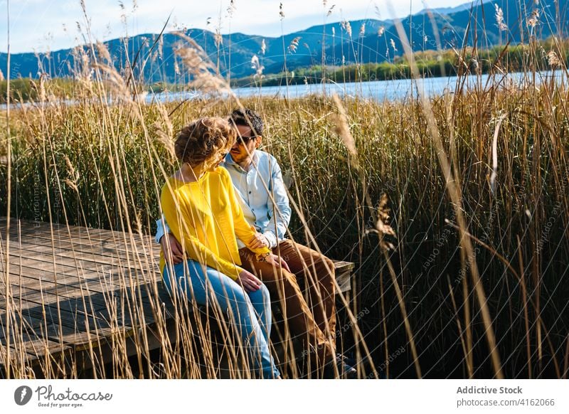 Ehepaar sitzt im Sommer auf einem Holzkai Paar Pier See Berge u. Gebirge Partnerschaft sich[Akk] entspannen Zusammensein Umarmung Sonnenlicht Liebe hölzern