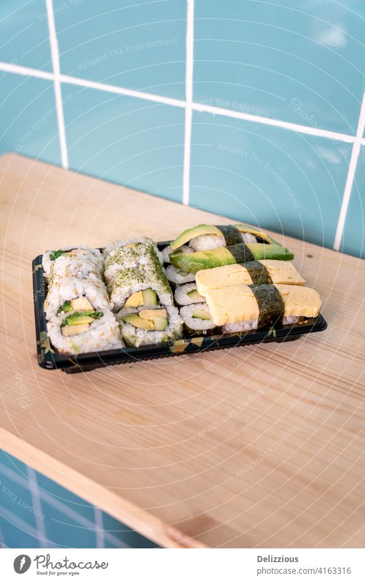 Frisches vegetarisches Sushi zum Mitnehmen auf hölzerner Oberfläche und blauem Kachelhintergrund Vegetarier Lebensmittel Hintergrund keine Menschen niemand