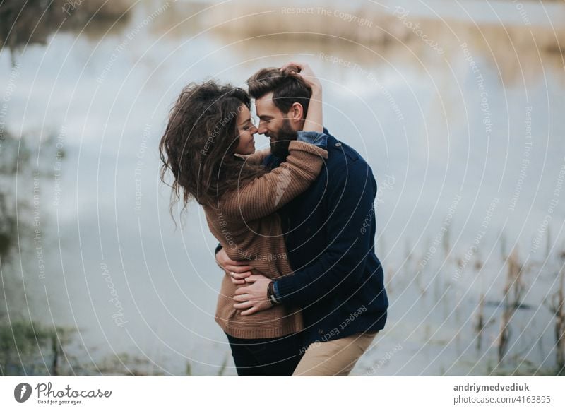 Zwei kaukasische Liebhaber in der Nähe des Sees. Junges Paar umarmt sich am Herbsttag im Freien. Ein bärtiger Mann und lockige Frau in der Liebe. Valentinstag. Konzept der Liebe